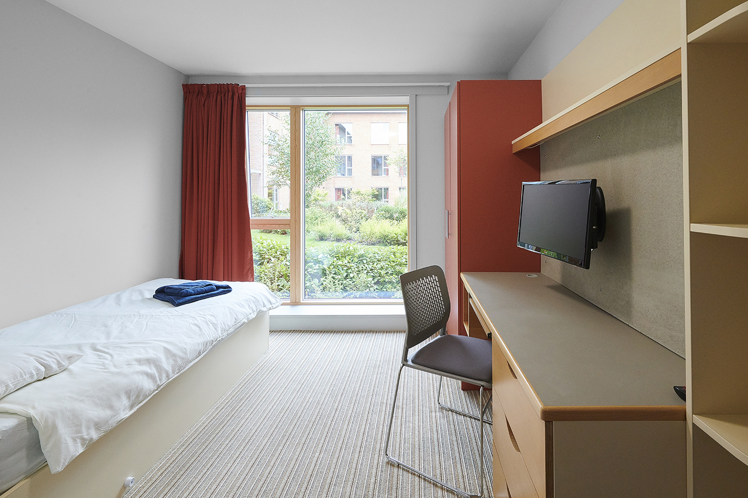 A bedroom furnished with a bed, desk, wardrobe, shelves and storage in a Founders hall of residence.