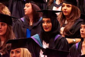 A student stands in the graduation hall during a graduation ceremony.