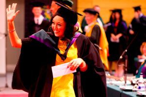 A graduate waves to family and friends in the audience as she walks along the red carpet after receiving her degree.