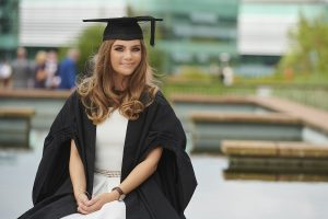 A graduate poses for a photo in the piazza area on the western side of campus.