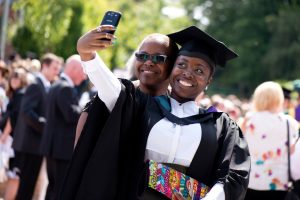 A graduate and their guest take a selfie after a graduation ceremony.