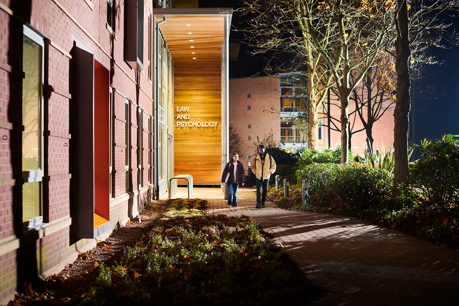 Two students walk outside the Law and Psychology building at night.