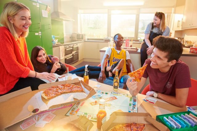 Five students eat pizza in the dining area of a hall of residence.