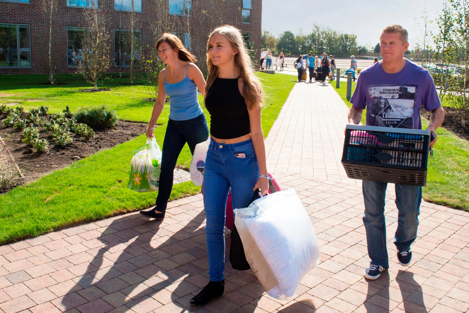 A student and her parents carry crates and bags as she prepares to move into her room on campus.