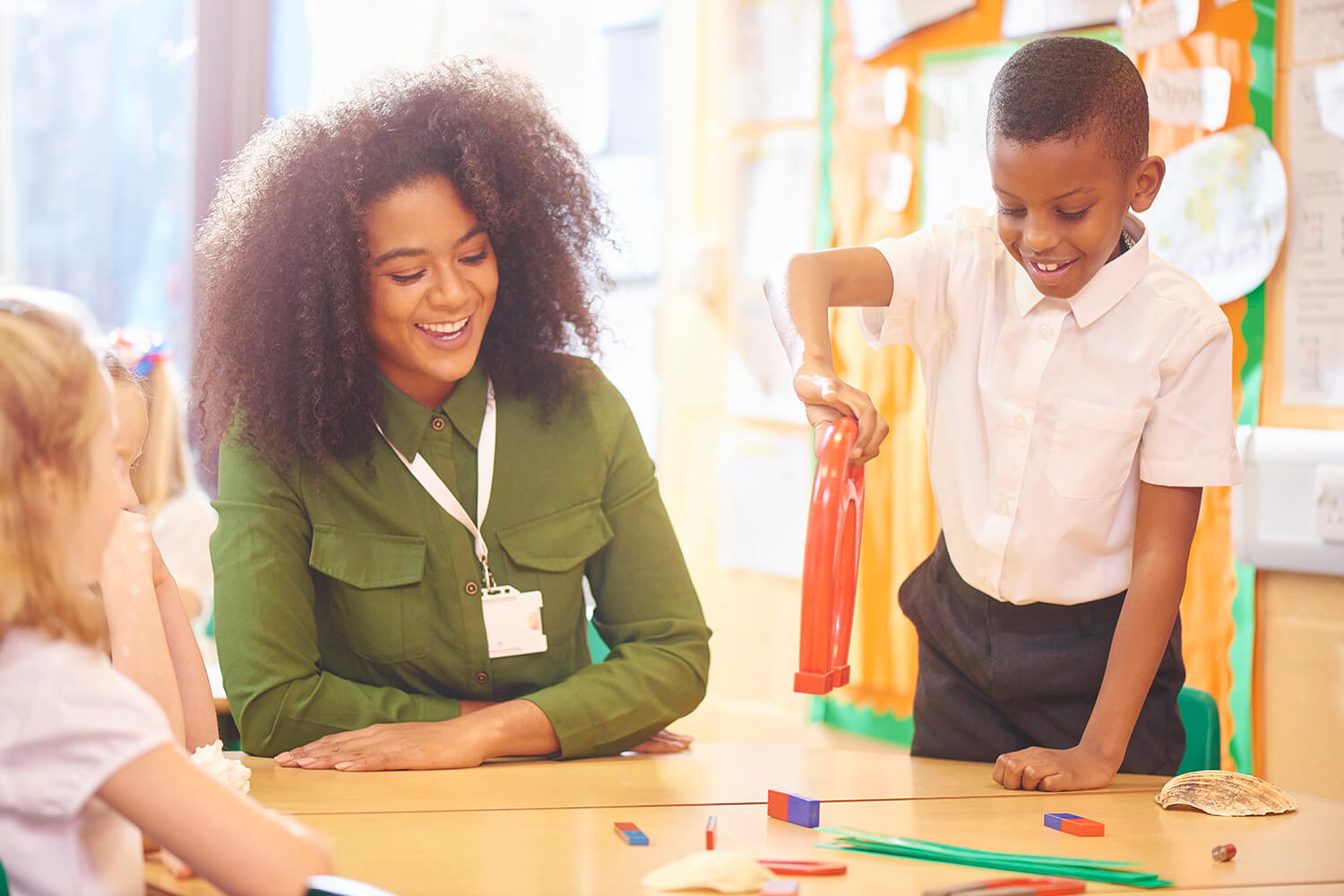 A teacher shows children how to pick up objects using a magnet during a lesson in a primary school classroom.