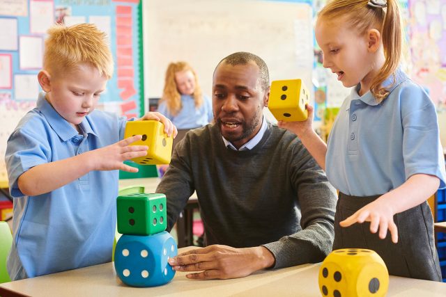 A teacher uses large dice with pupils during a lesson in a primary school classroom.