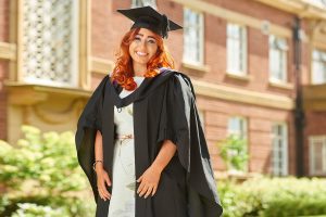 A graduate, wearing their cap and gown, walks past the Main Building on graduation day.