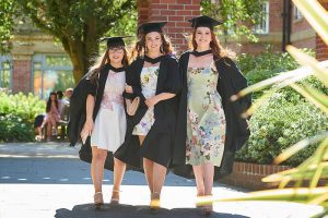 Three graduates walk near the Hub and Main Building in their graduation robes and mortar boards.