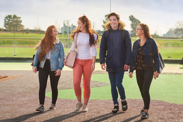 Four students walk together on the viewing platform on the roof of the Sports Centre which overlooks the athletics track.