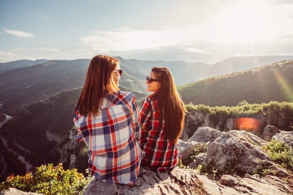 Two students enjoy a stunning panorama of mountains around them while sitting on rocks during a walk.