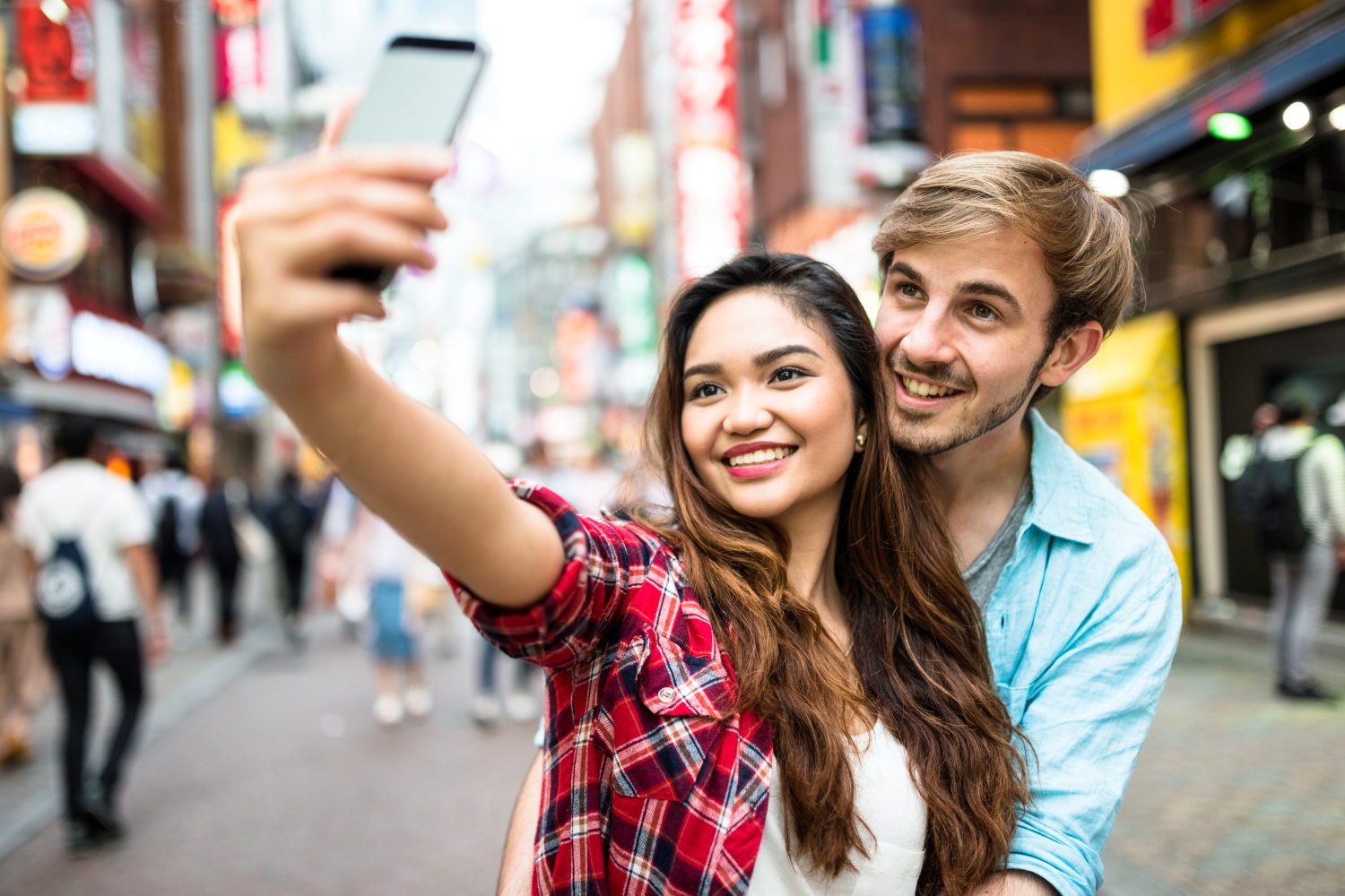 Two students pause to take a selfie in a busy street in Asia.