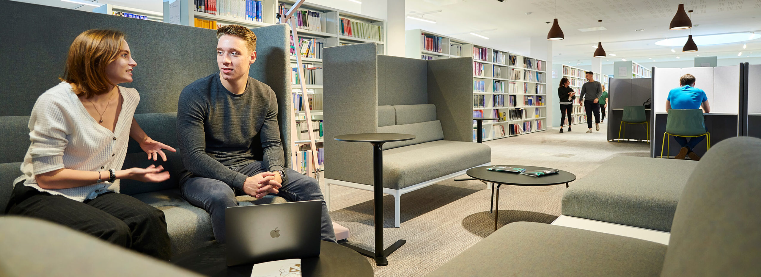 Two students chat while sat on a sofa in the University library.