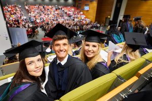 Three graduands sit in a lecture theatre prior to the start of their graduation ceremony.