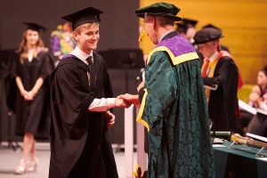 A graduand shakes the hand of Dr John Cater during a graduation ceremony.