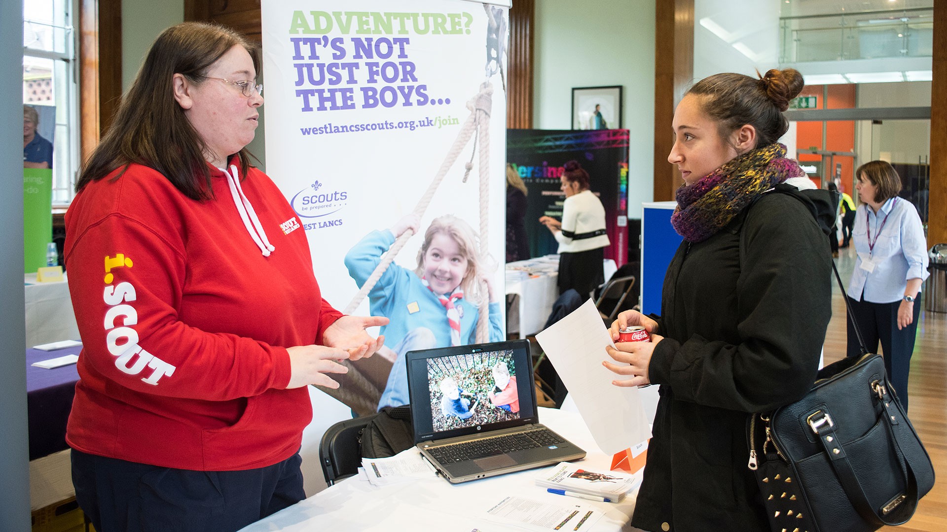 An image of two people talking at a desk at a careers fair.