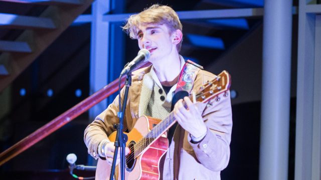 An image of a person playing a guitar and singing into a microphone in the Arts Centre on the Edge Hill University campus.