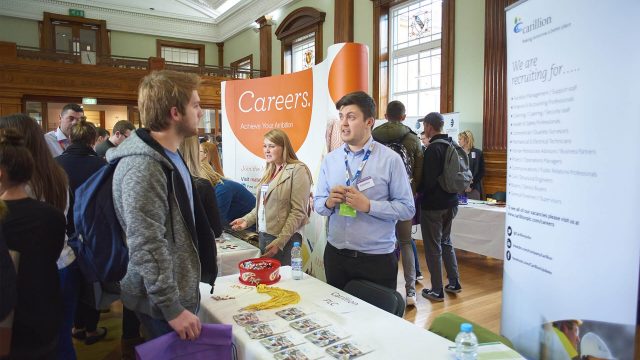 In this image there is a careers fair taking place on the Edge Hill University campus. This image focuses on one student talking to an employer. 