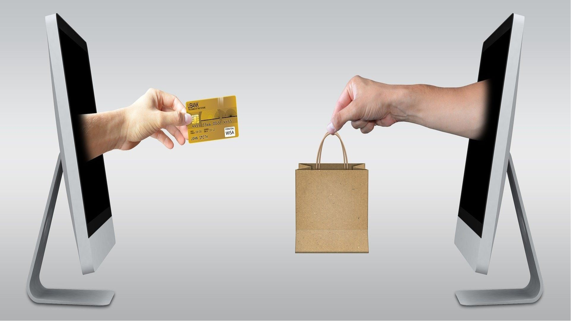 An image of two hands coming out of two seperate computer screens. One is holding a golden credit card, the other is holding a paper shopping bag.