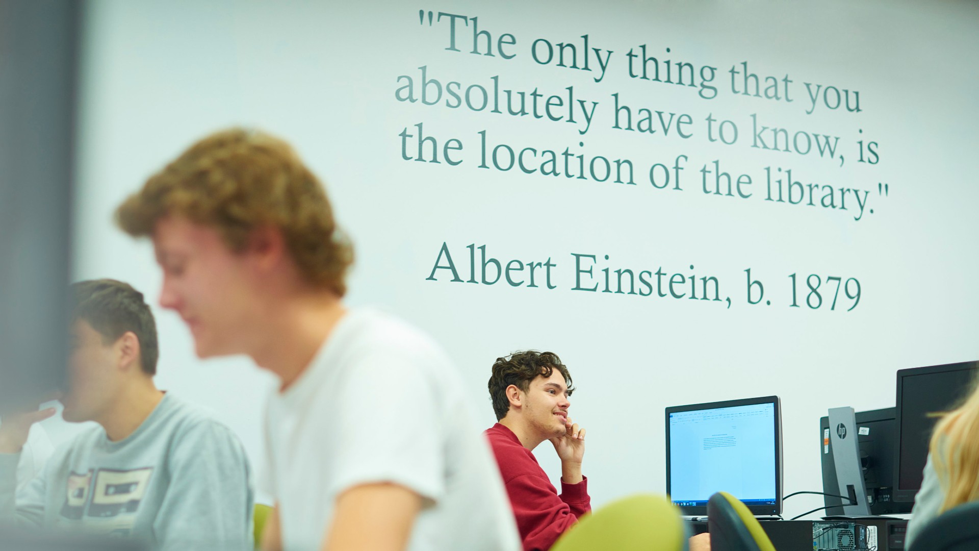 A photo of people sat at computers in front of a sign on the wall that quotes Albert Einstein. 