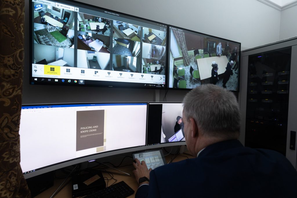 4 PC screens with CCTV of footage from rooms across the building being looked at by policing academic.
