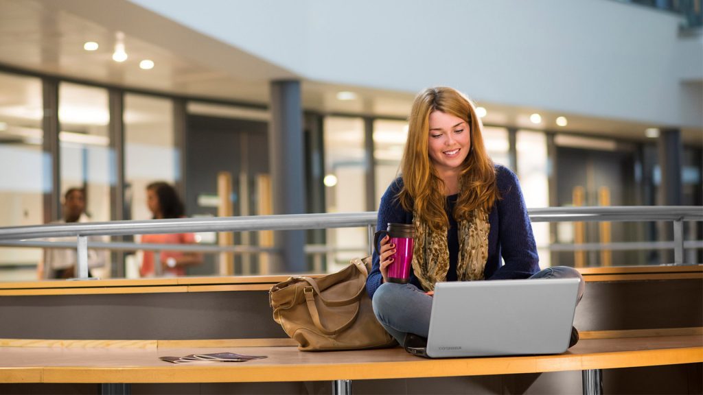 A student sat cross legged with a laptop on their knee