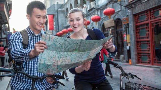 Two people are on bikes in the centre of a town. They are looking at a map that they are both holding.
