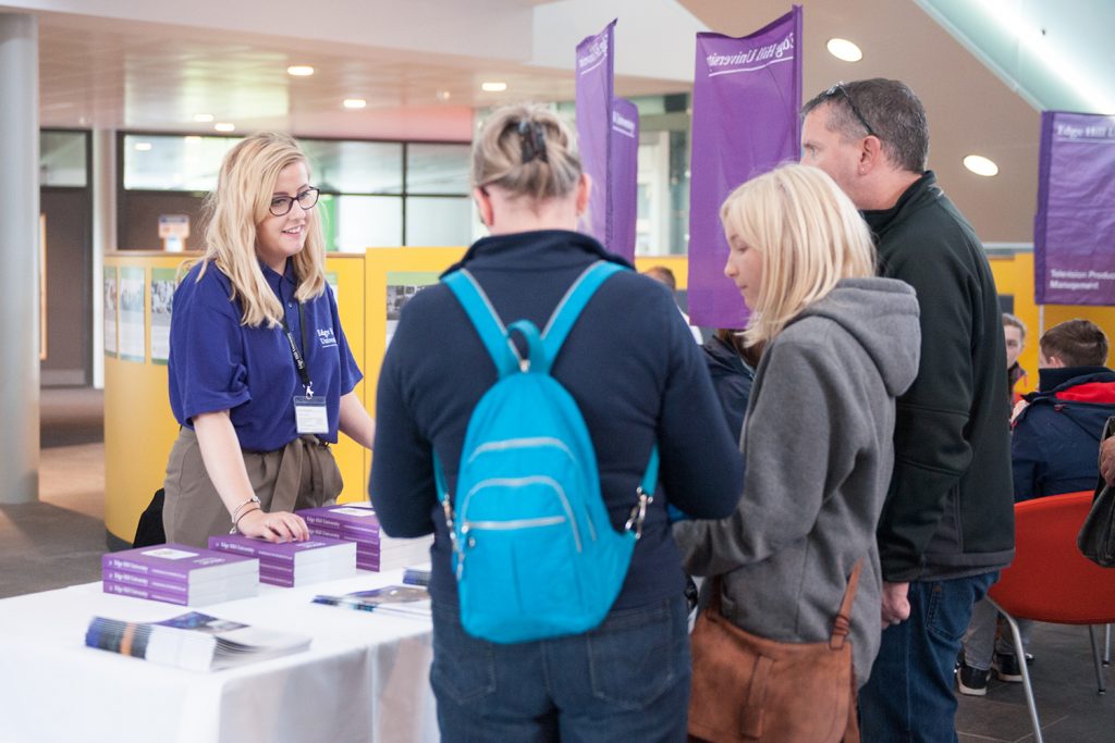 A prospective student and their parents talk with a member of Edge Hill staff stood at an information point at an Applicant Visit Day