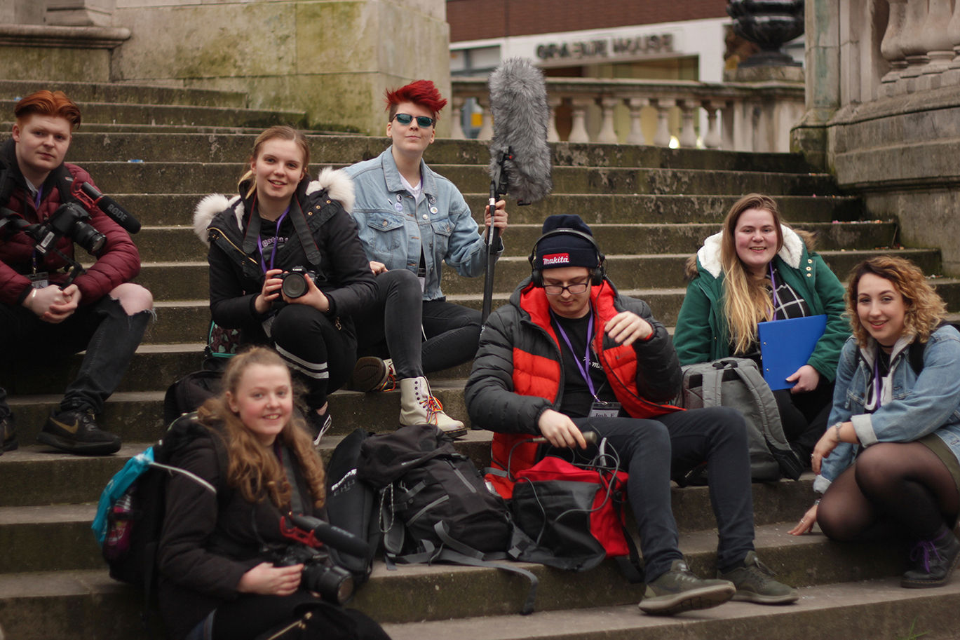 Olivia Egmore and the crew for her documentary project sit on a flight of steps with their filming equipment.