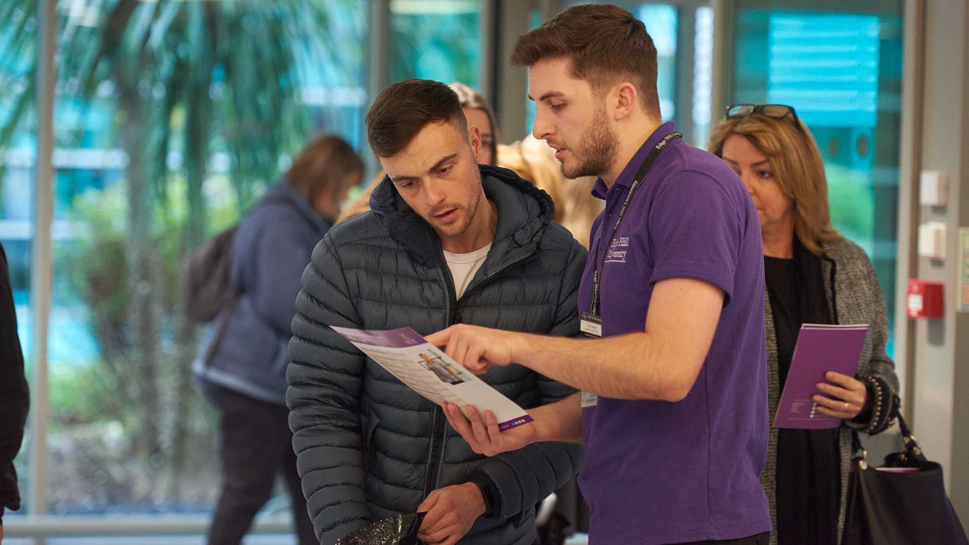 Staff explaining a course leaflet to a student. The staff member is wearing an Edge Hill tabard