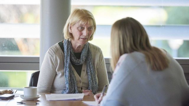 Two women talking at a table, one woman is making notes