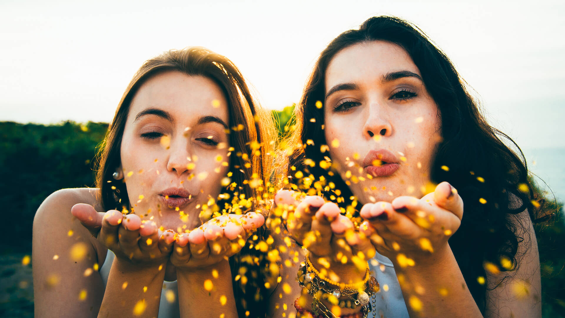 Two students blow gold glitter at the camera