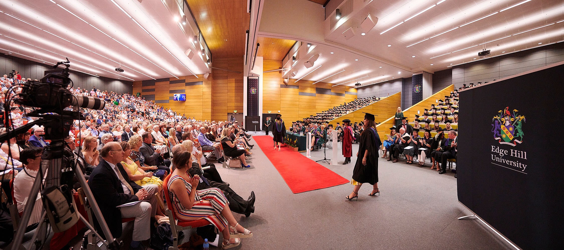 A graduand waits at the start of the red carpet to receive their award during a graduation ceremony.