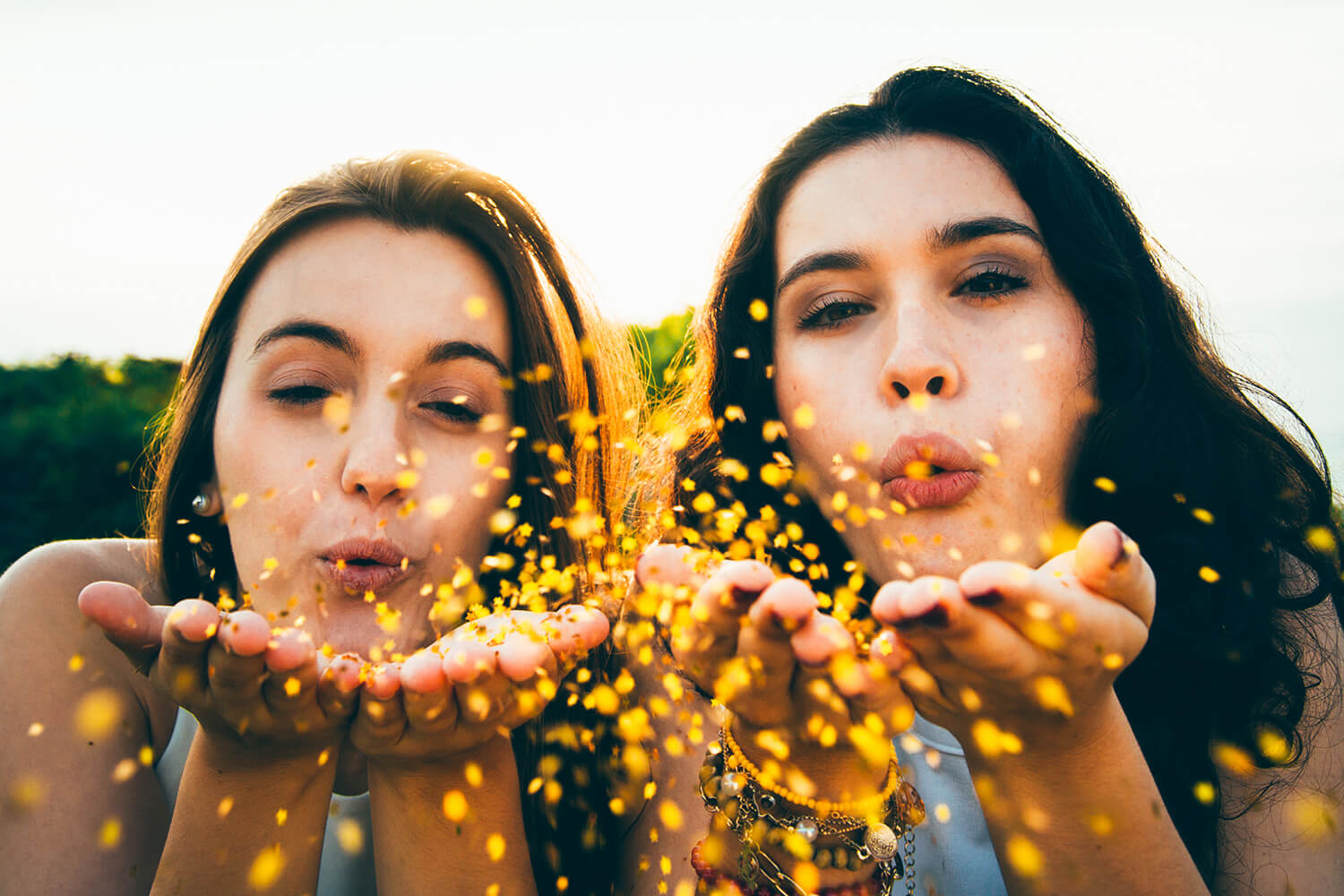 Two students in the countryside blowing glitter from their hands.