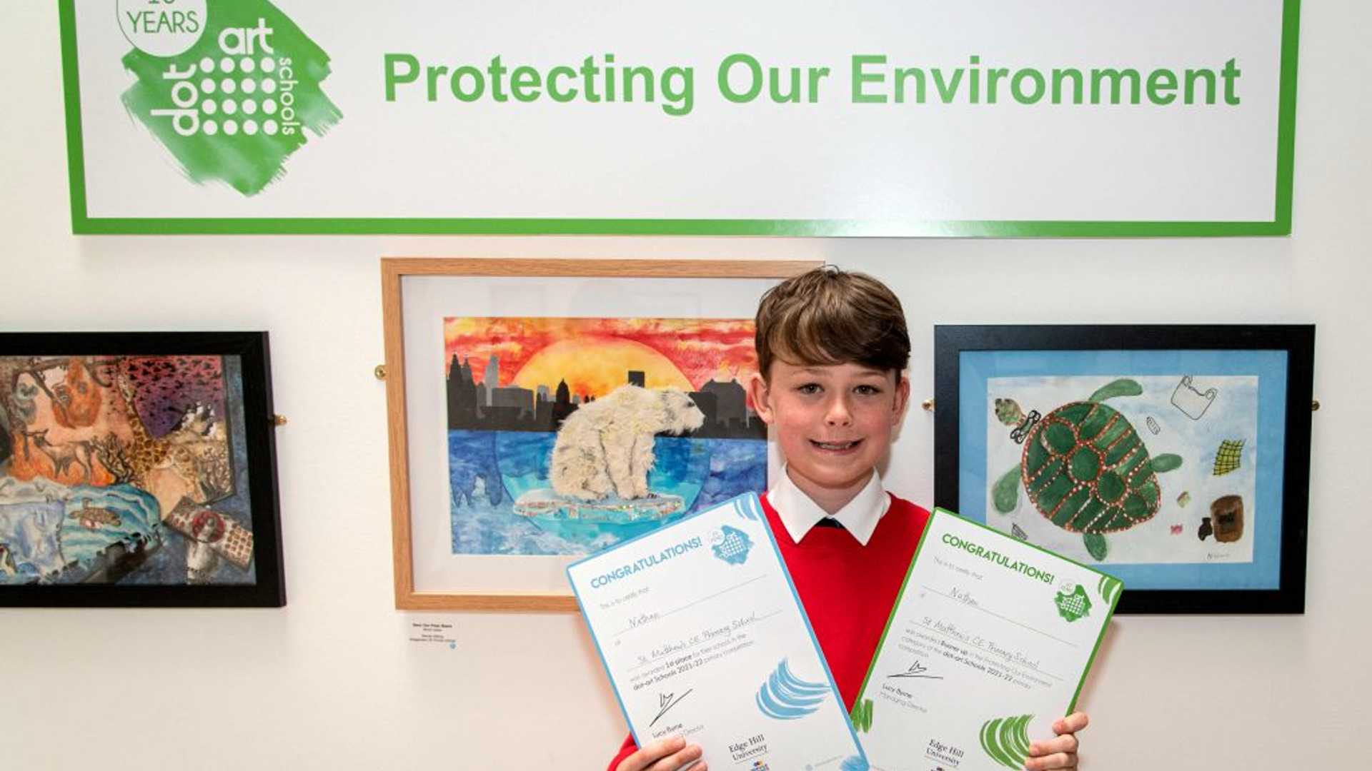 One of the dot art school art competition winners holding two certificates and looking pleased.