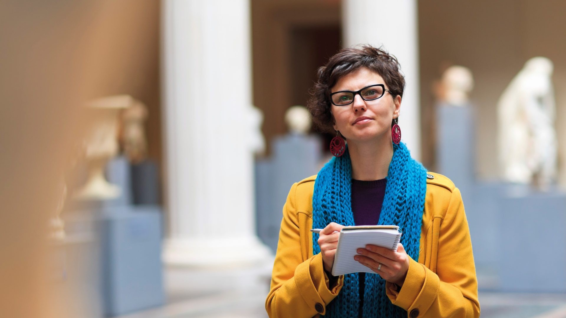 An image of a person writing something into a notebook whilst looking at an exhibit in a museum.