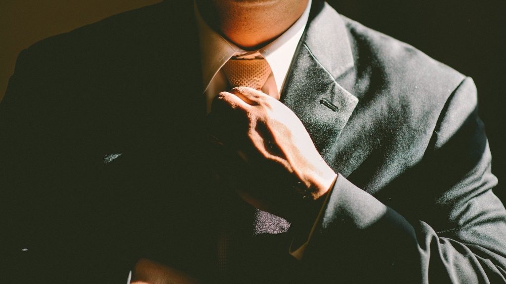 An image of a person fixing an orange tie that they are wearing.