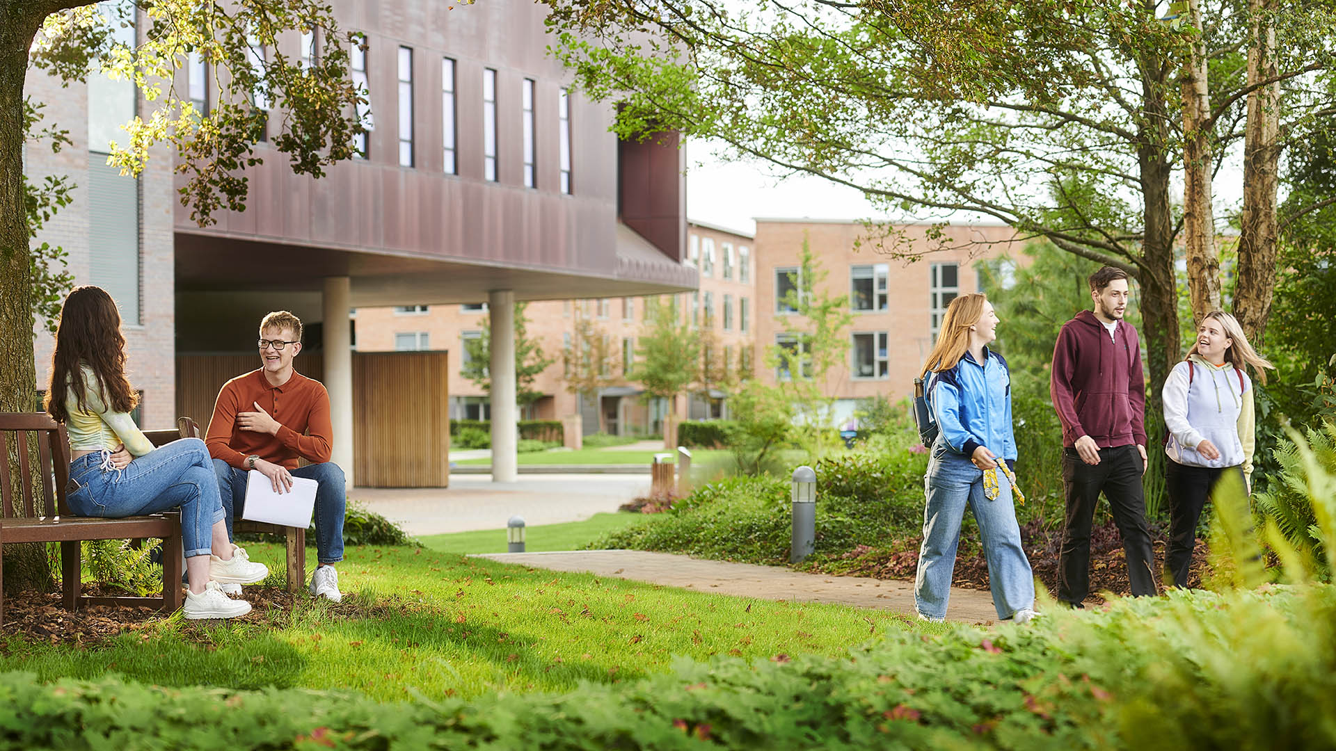 Outside our Catalyst building, a couple of students relax on a bench while another group walk across campus