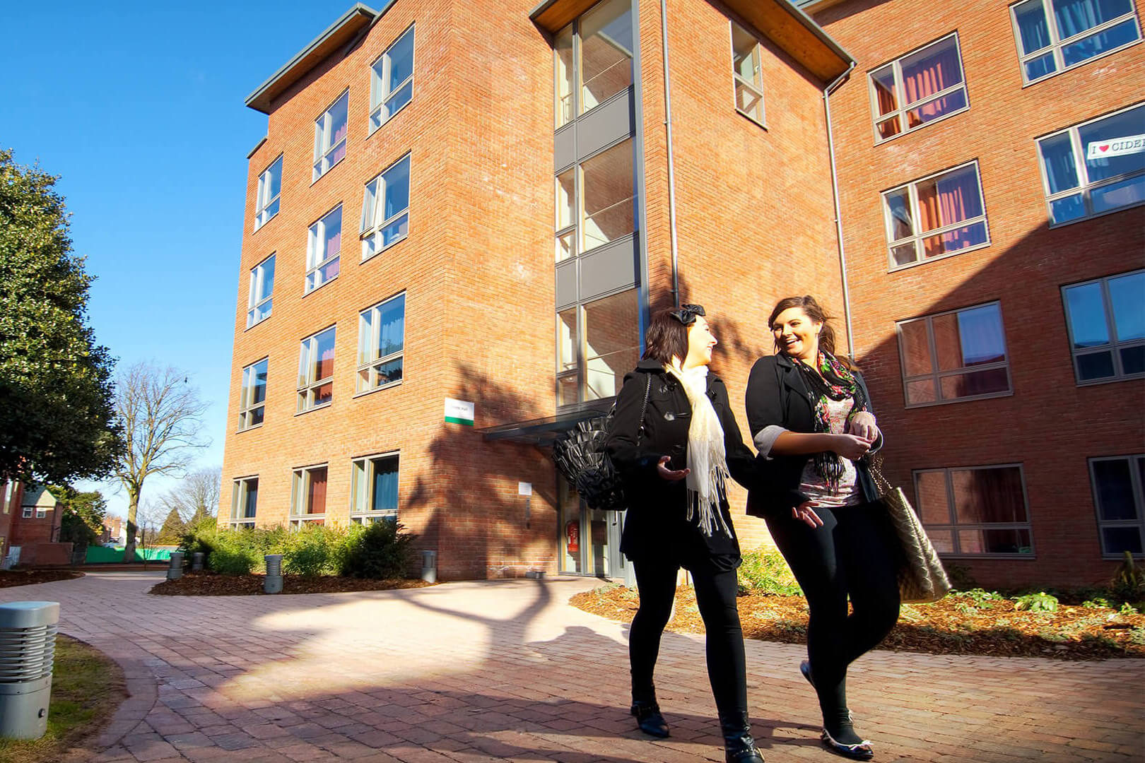 An image of two people walking past one of the accomodation blocks at Edge Hill University. The image is set in the day.