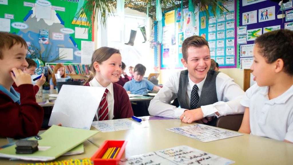 A teacher is sat with a group of students at a table.