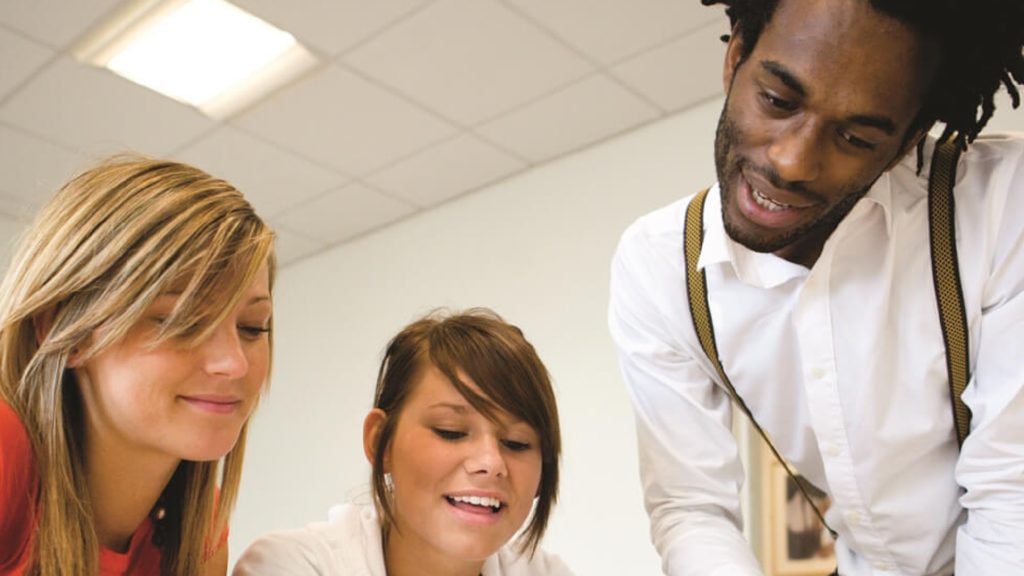 Three students are looking at something on a table.