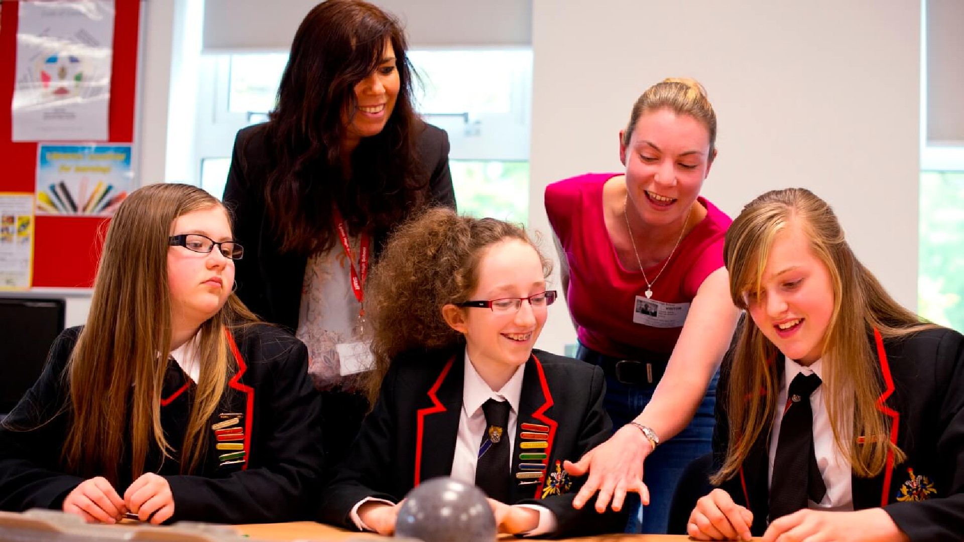 Two teachers are helping a group of students at a table.