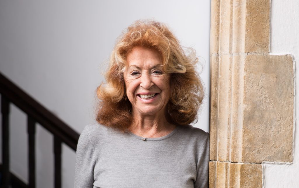 Lynda La Plante smiles at the camera while leaning against a stone wall.
