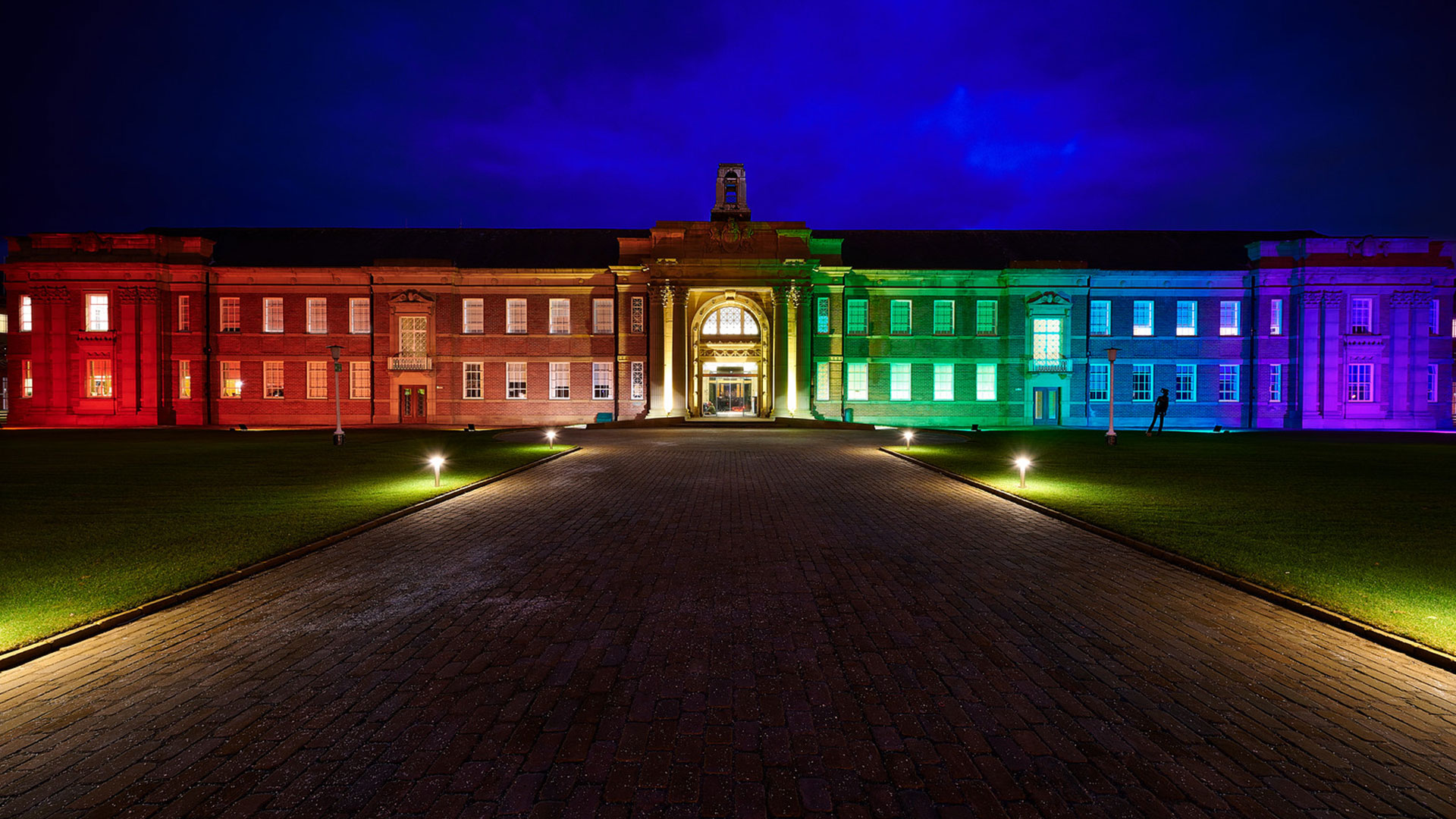 Main building at night lit up in the colours of the rainbow