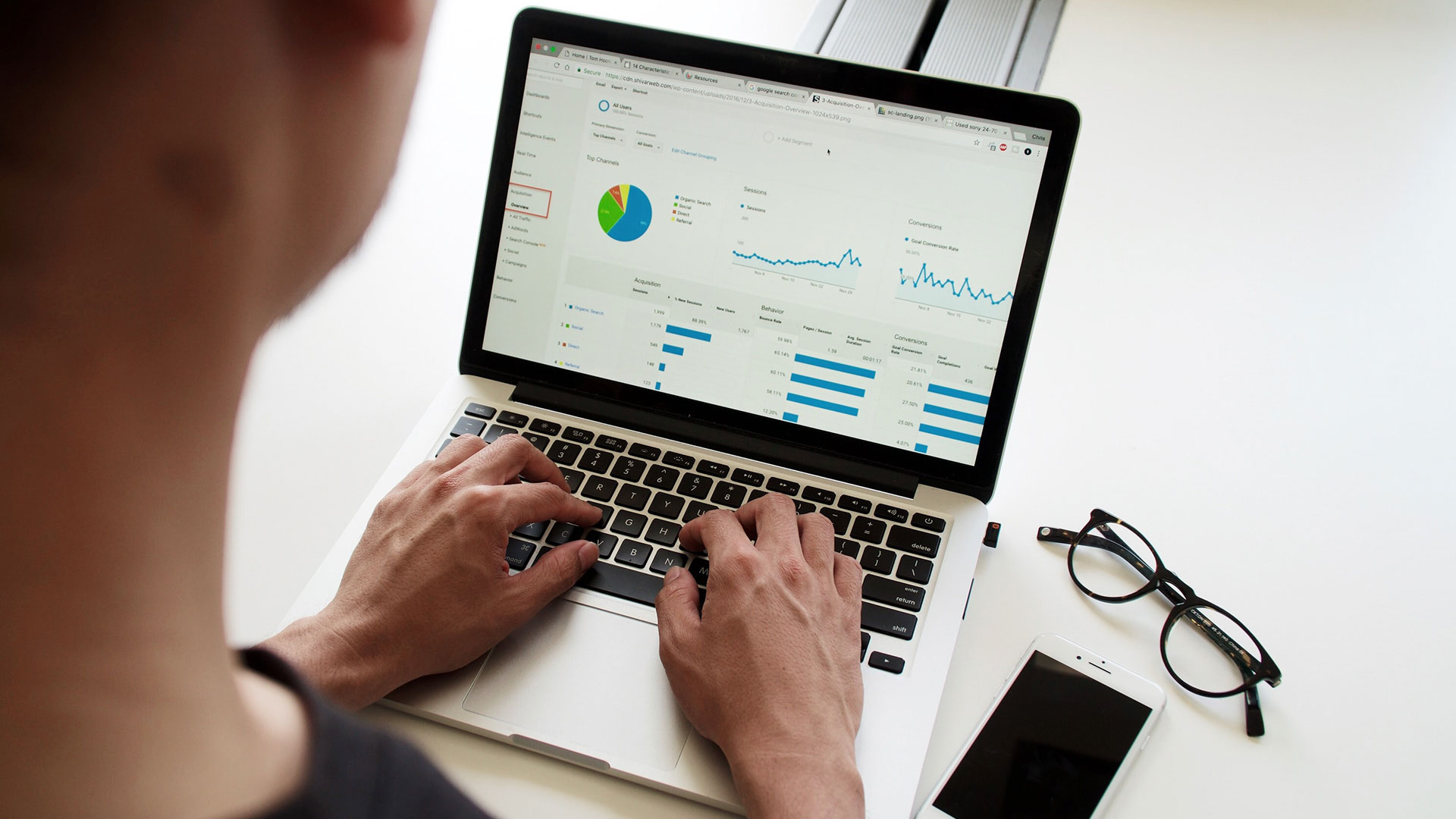 mage over the shoulder of a person viewing a laptop screen which includes some graphs on