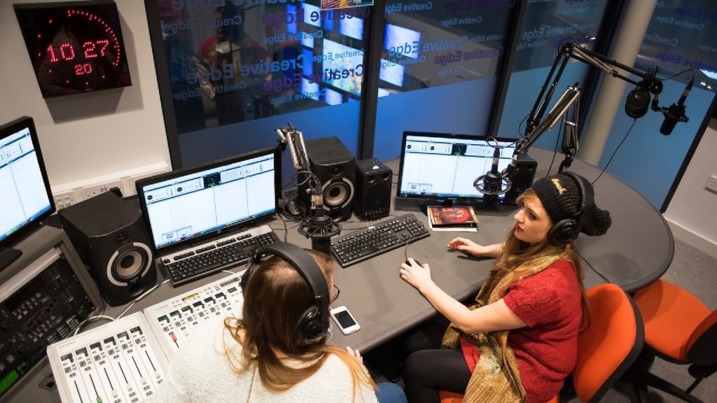 An image of two students sat in a radio station on the Edge Hill University campus within the Creative Edge building.