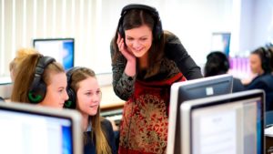 A teacher and two pupils listen on headphones to audio from a computer.