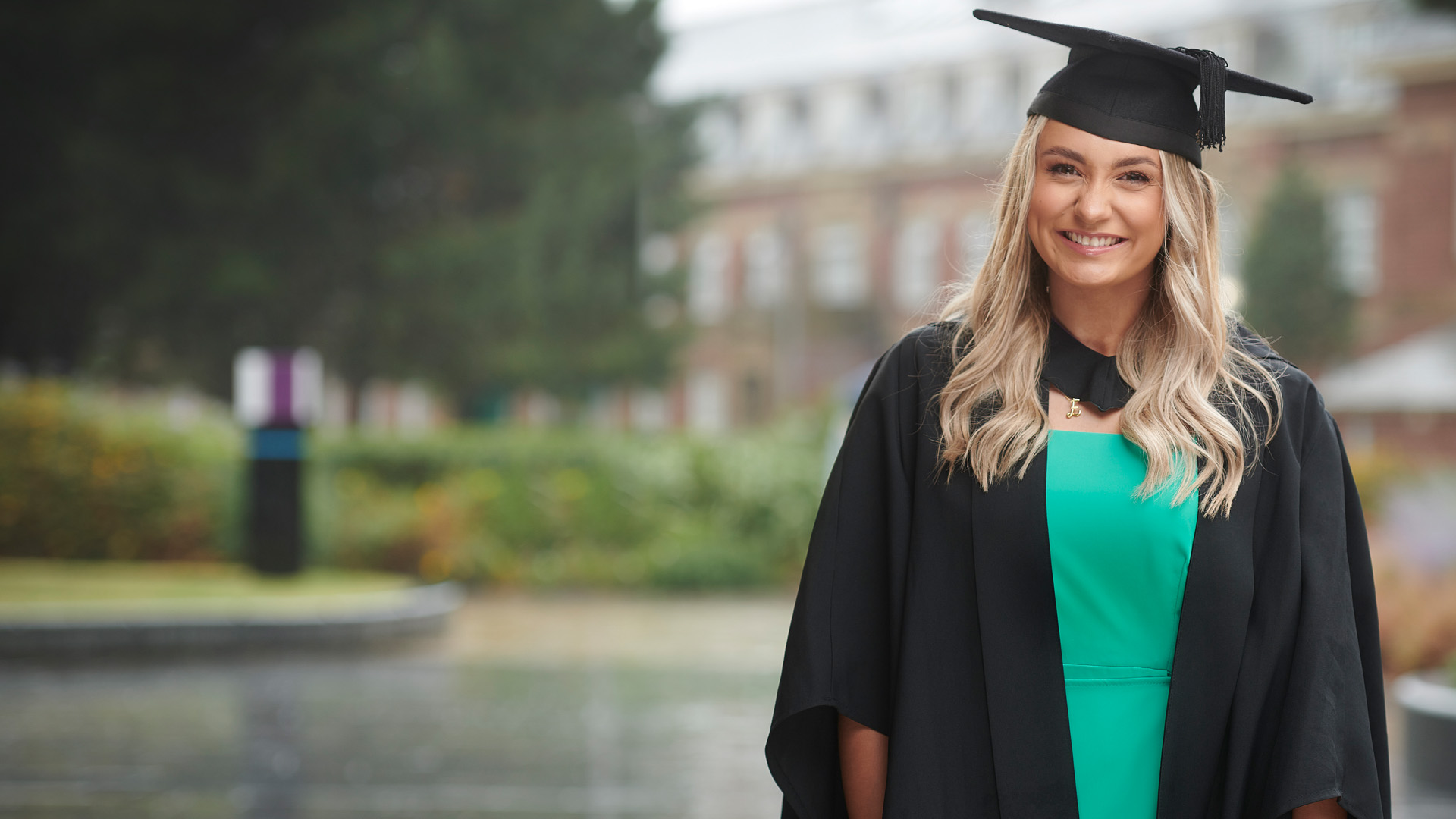 anna bolger wearing a green dress and a cap and gown at graduation.