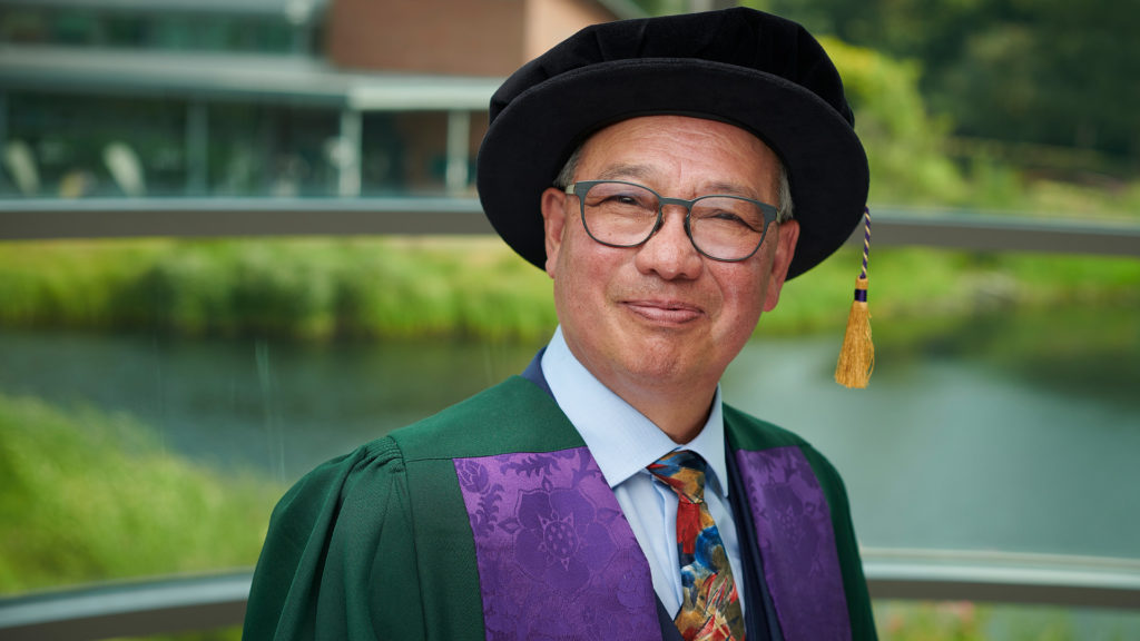 David Yip wearing green and purple robes at their honorary graduation.