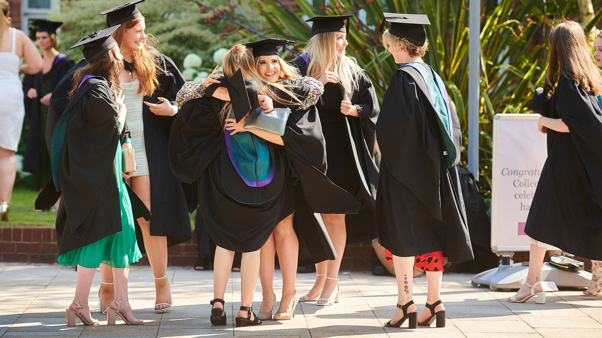 A group of graduates celebrating and hugging each other, whilst wearing their graduation cap and gowns.