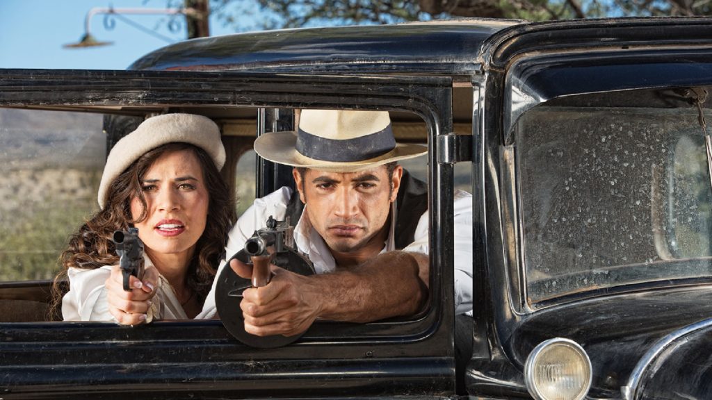 An image of two people in a car, they are both holding guns out of the car window.